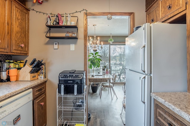 kitchen featuring pendant lighting, white appliances, wood-type flooring, and an inviting chandelier