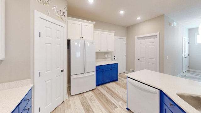 kitchen with blue cabinets, white cabinets, white appliances, and light hardwood / wood-style flooring