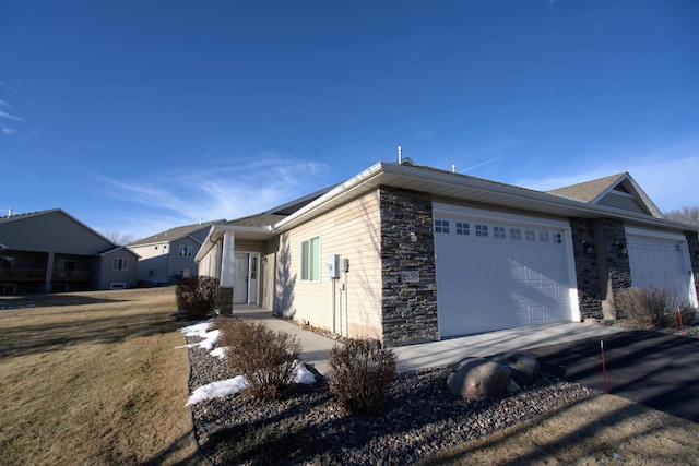 view of side of property featuring a garage, stone siding, and asphalt driveway