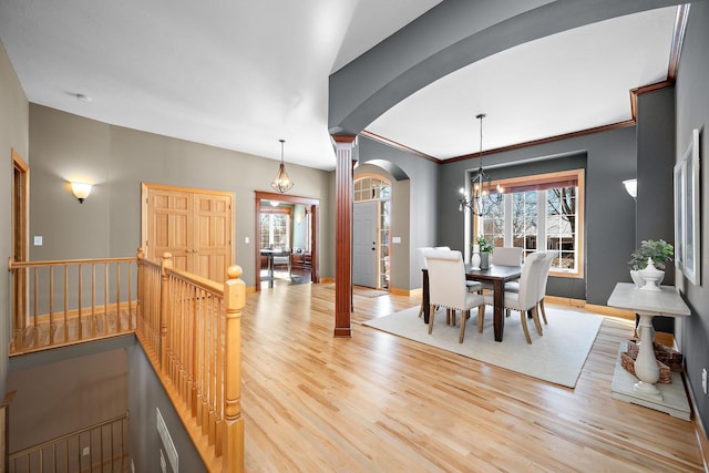 dining space featuring crown molding, a notable chandelier, ornate columns, wood finished floors, and baseboards