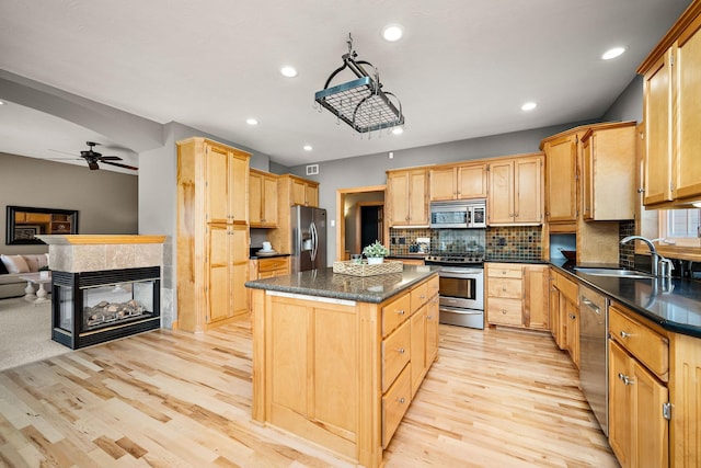 kitchen with appliances with stainless steel finishes, open floor plan, a center island, light brown cabinets, and a sink