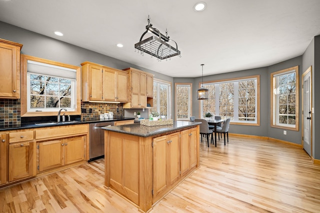 kitchen with a kitchen island, a sink, stainless steel dishwasher, dark countertops, and decorative light fixtures