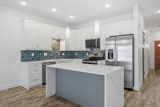 kitchen with appliances with stainless steel finishes, white cabinets, hanging light fixtures, a center island, and light wood-type flooring