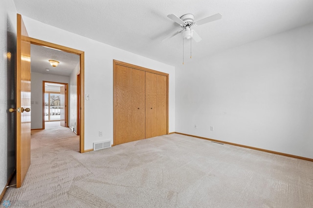 unfurnished bedroom with light carpet, a textured ceiling, a closet, and ceiling fan