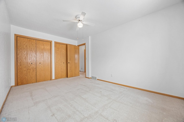 unfurnished bedroom with multiple closets, ceiling fan, and light colored carpet