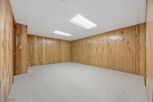 basement featuring carpet floors, a drop ceiling, and wood walls