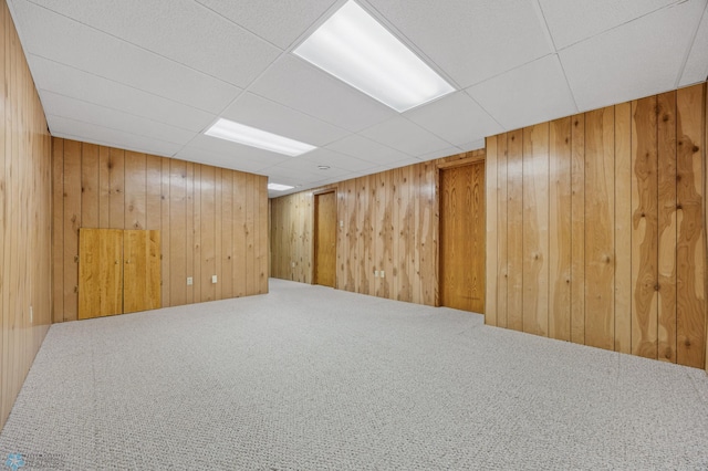 basement with carpet, a paneled ceiling, and wood walls