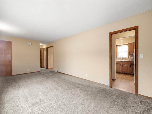 empty room featuring light carpet, baseboards, visible vents, and a sink