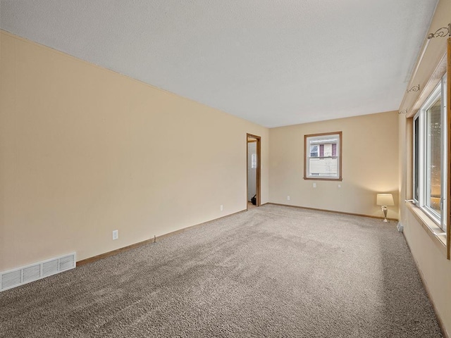 spare room featuring light carpet, visible vents, and baseboards