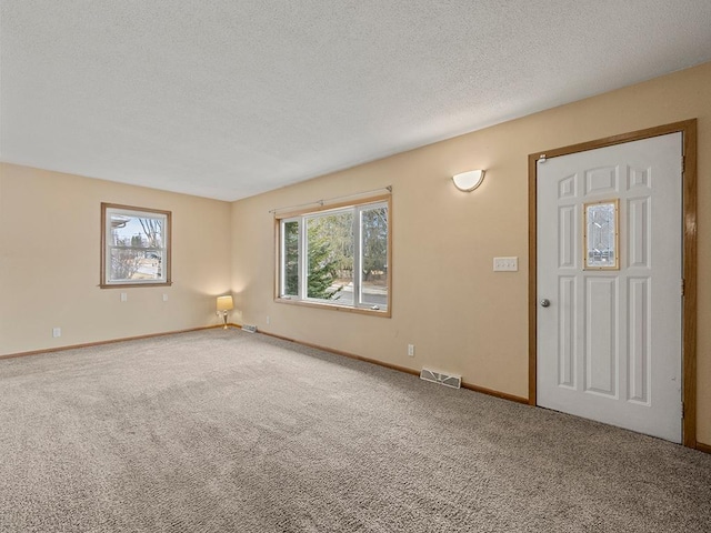 carpeted empty room featuring baseboards, a textured ceiling, visible vents, and a wealth of natural light