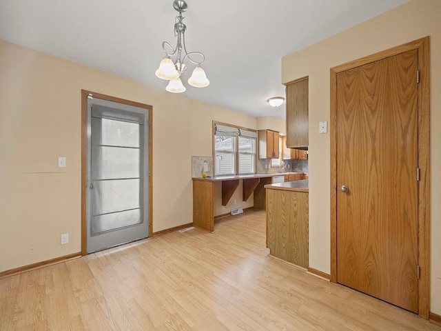 kitchen with brown cabinetry, light wood-type flooring, a chandelier, and baseboards