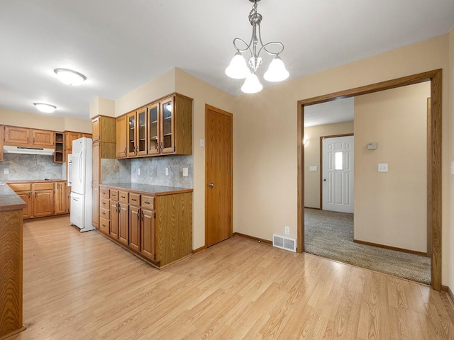 kitchen with light wood finished floors, visible vents, brown cabinetry, freestanding refrigerator, and under cabinet range hood