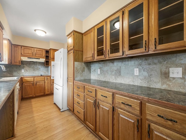 kitchen featuring light wood-style flooring, brown cabinetry, freestanding refrigerator, and under cabinet range hood