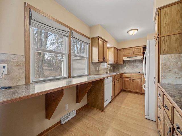 kitchen with under cabinet range hood, white appliances, a sink, visible vents, and light wood-style floors