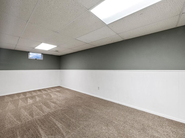 below grade area with a paneled ceiling, a wainscoted wall, and carpet flooring