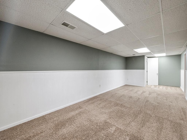 finished basement featuring a paneled ceiling, carpet, visible vents, and wainscoting