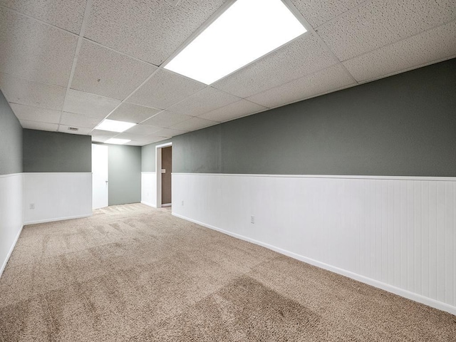 finished basement featuring a wainscoted wall, carpet, and a drop ceiling