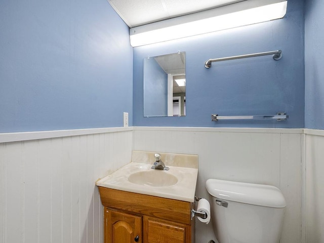 half bath with toilet, wainscoting, and vanity