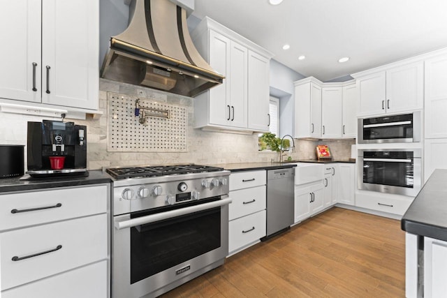 kitchen with sink, light hardwood / wood-style flooring, premium range hood, white cabinetry, and appliances with stainless steel finishes