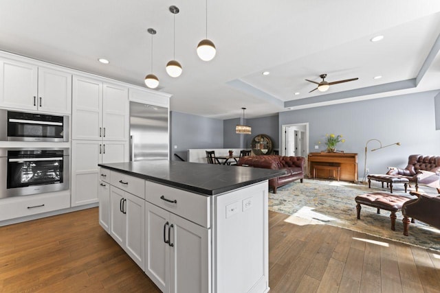 kitchen with white cabinetry, decorative light fixtures, a center island, appliances with stainless steel finishes, and a raised ceiling