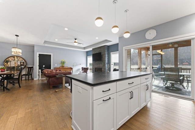 kitchen with decorative light fixtures, a raised ceiling, light wood-type flooring, and white cabinets