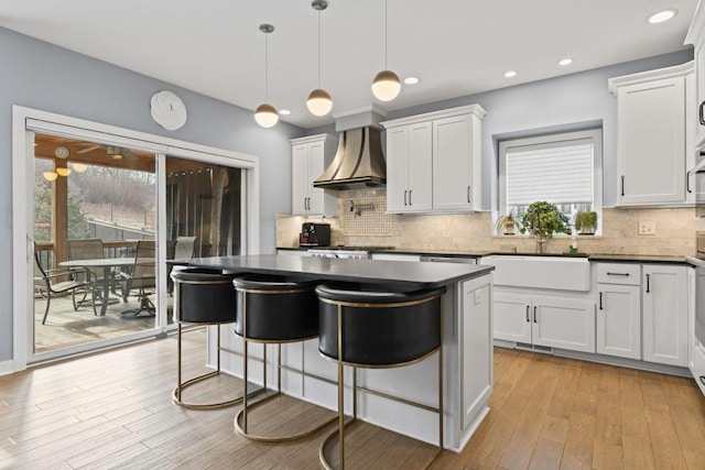 kitchen featuring sink, light hardwood / wood-style flooring, premium range hood, white cabinets, and decorative light fixtures