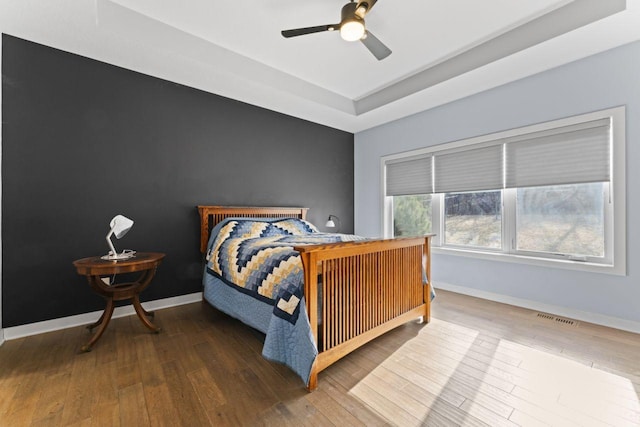 bedroom featuring ceiling fan, wood-type flooring, and a tray ceiling