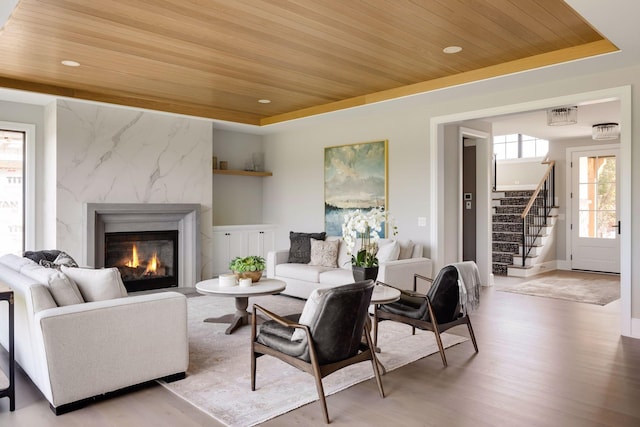 living room featuring light wood-type flooring, a high end fireplace, wood ceiling, and a tray ceiling