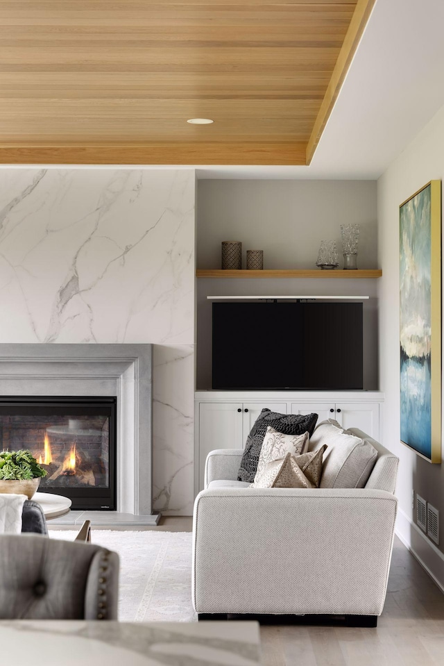 living room with a raised ceiling, wooden ceiling, and a high end fireplace