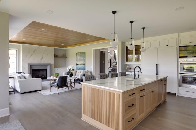 kitchen with sink, a kitchen island with sink, a fireplace, decorative light fixtures, and stainless steel double oven