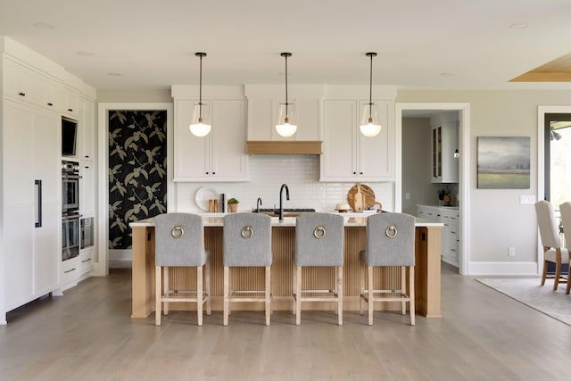 kitchen with white cabinetry, decorative light fixtures, a kitchen island with sink, and backsplash