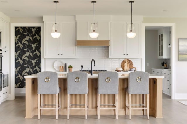 kitchen featuring sink, white cabinetry, a center island with sink, tasteful backsplash, and a kitchen bar