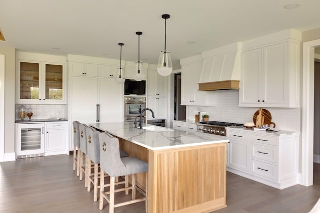 kitchen featuring appliances with stainless steel finishes, sink, wine cooler, a kitchen island with sink, and light stone countertops