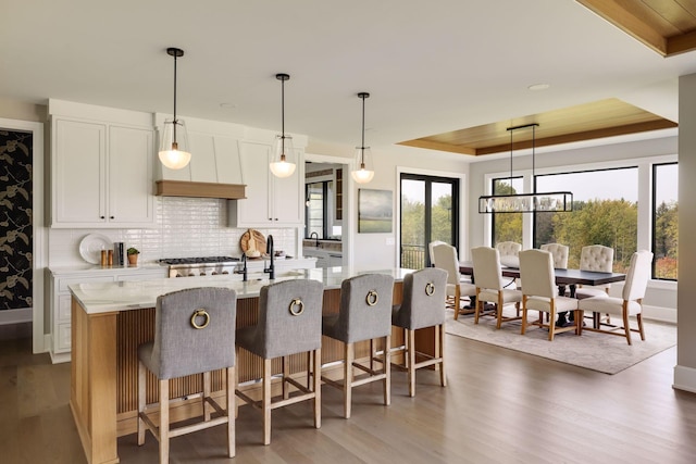 kitchen with hanging light fixtures, a large island with sink, a tray ceiling, light stone countertops, and white cabinets