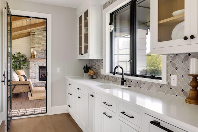 bar featuring a stone fireplace, sink, white cabinets, dark hardwood / wood-style flooring, and decorative backsplash