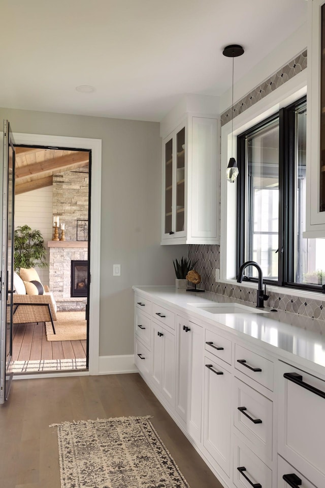 kitchen with a stone fireplace, sink, dark hardwood / wood-style floors, pendant lighting, and white cabinets