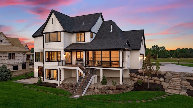 back house at dusk featuring a lawn