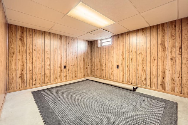 basement featuring a paneled ceiling and wood walls