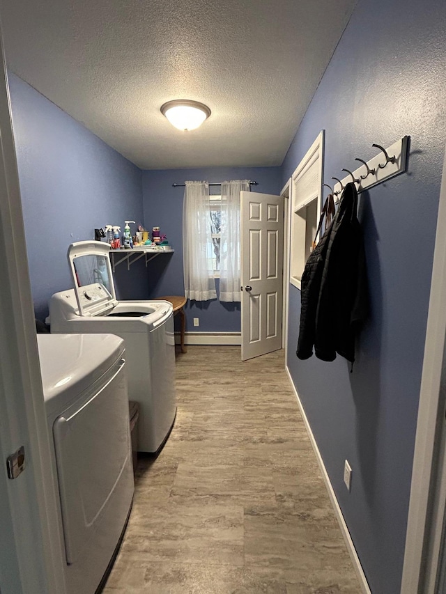 clothes washing area featuring a baseboard heating unit, washing machine and dryer, a textured ceiling, and light wood-type flooring