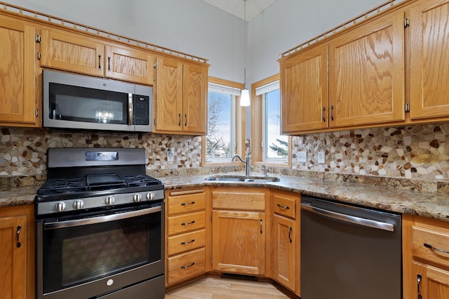 kitchen featuring sink, light stone counters, light hardwood / wood-style flooring, stainless steel appliances, and backsplash