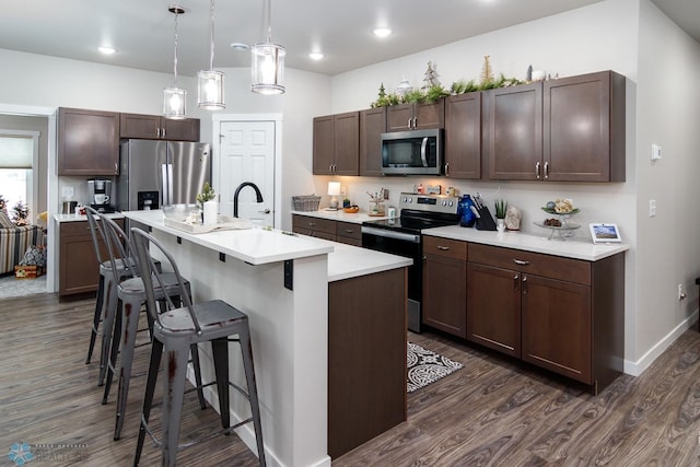 kitchen with a kitchen bar, dark hardwood / wood-style floors, pendant lighting, stainless steel appliances, and a kitchen island with sink