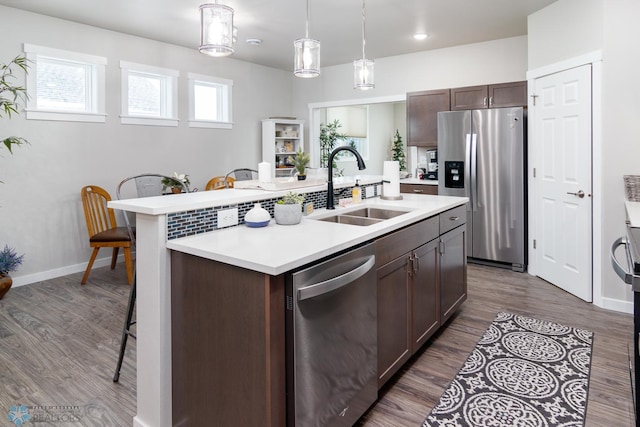 kitchen with sink, decorative light fixtures, dark brown cabinets, appliances with stainless steel finishes, and a kitchen island with sink