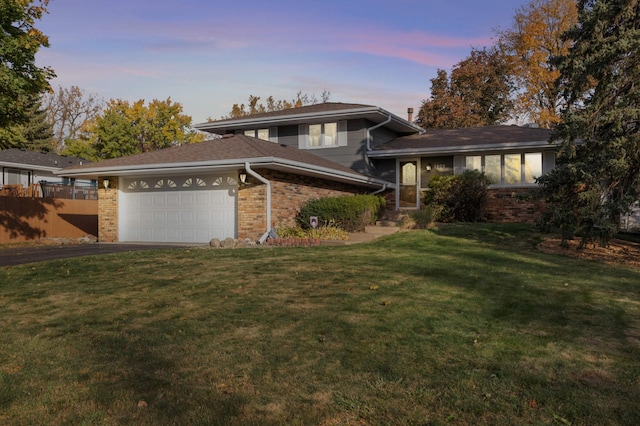 view of front facade with brick siding, fence, aphalt driveway, a garage, and a yard