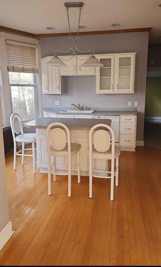 kitchen featuring a breakfast bar, pendant lighting, sink, white cabinets, and light hardwood / wood-style flooring