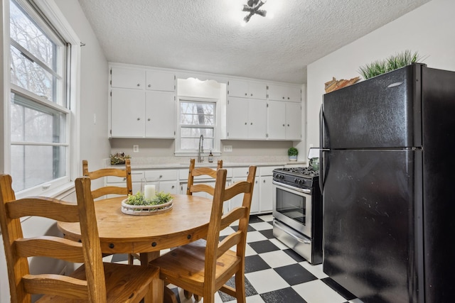 kitchen with sink, stainless steel gas range, white cabinetry, plenty of natural light, and black fridge