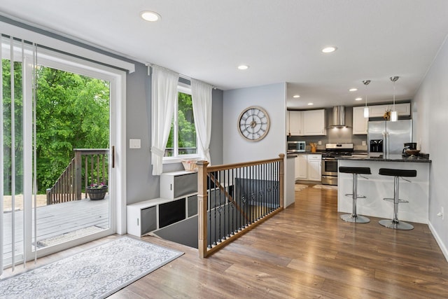 1524 Mulberry St, Taylors Falls, MN 55084 - kitchen featuring appliances with stainless steel finishes, dark countertops, wall chimney exhaust hood, wood finished floors, and a kitchen bar