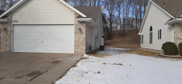 view of snowy exterior featuring central AC and a garage