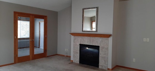 unfurnished living room featuring a tiled fireplace, light carpet, and french doors