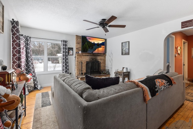 living room featuring a brick fireplace, hardwood / wood-style flooring, a textured ceiling, and ceiling fan