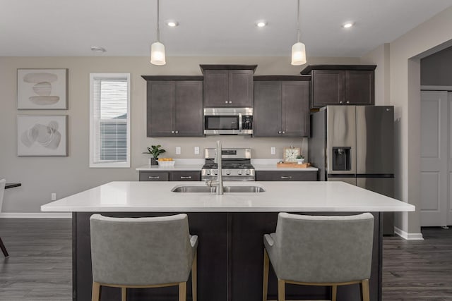 kitchen featuring hanging light fixtures, dark brown cabinets, a center island with sink, and appliances with stainless steel finishes